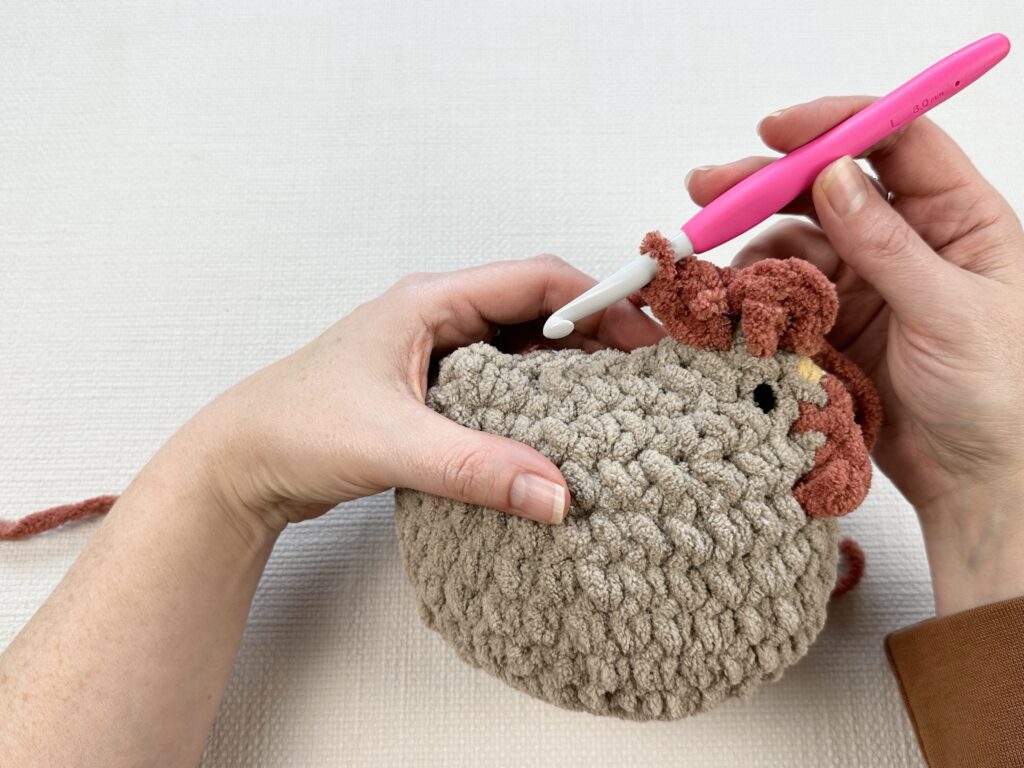 Hands crocheting a rooster modification onto the original Mabel chicken pattern. 