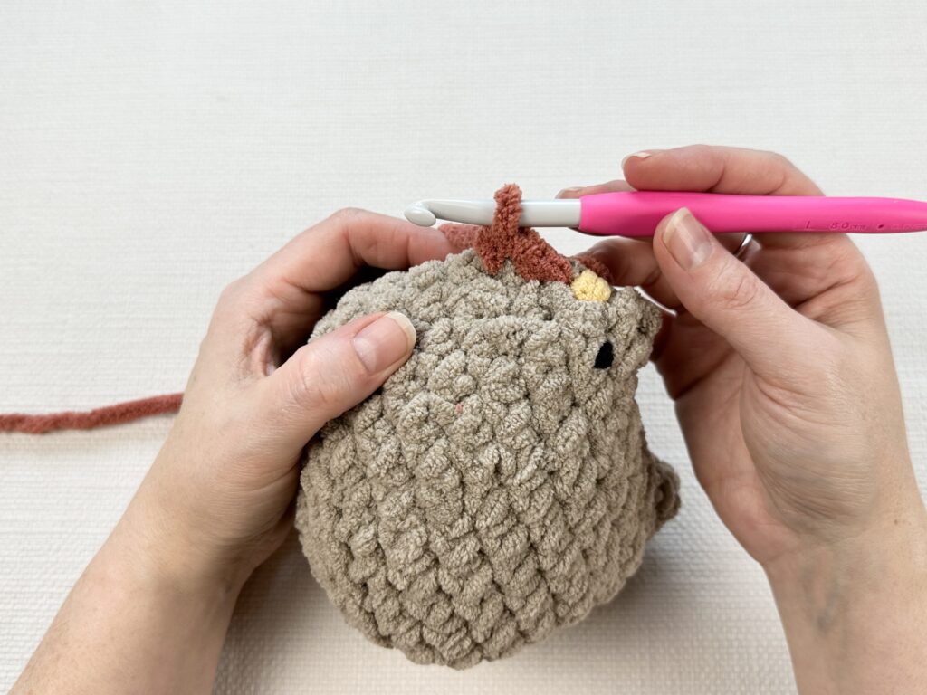 Hands crocheting a rooster modification onto the original Mabel chicken pattern. 