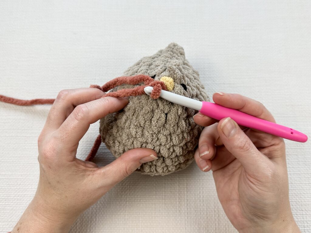 Hands crocheting a rooster modification onto the original Mabel chicken pattern. 