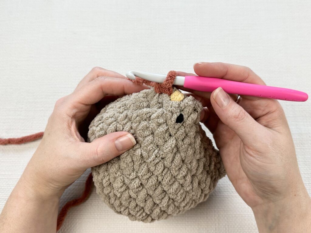 Hands crocheting a rooster modification onto the original Mabel chicken pattern. 