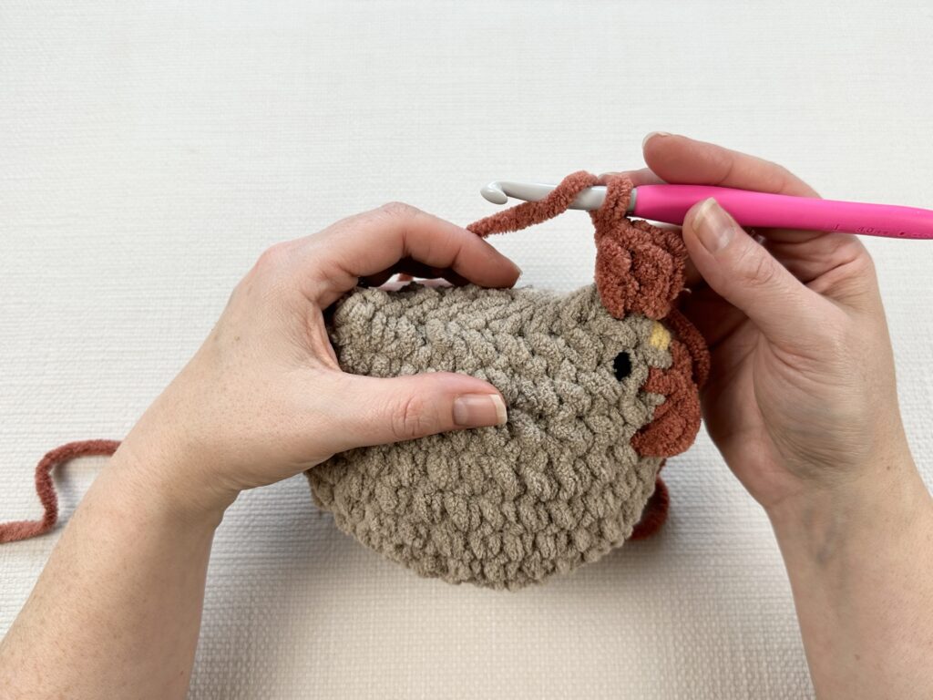 Hands crocheting a rooster modification onto the original Mabel chicken pattern. 