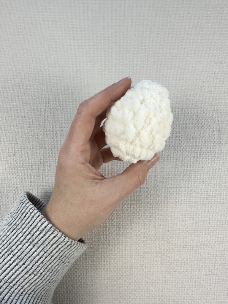 Hands showing a finished crochet egg. 