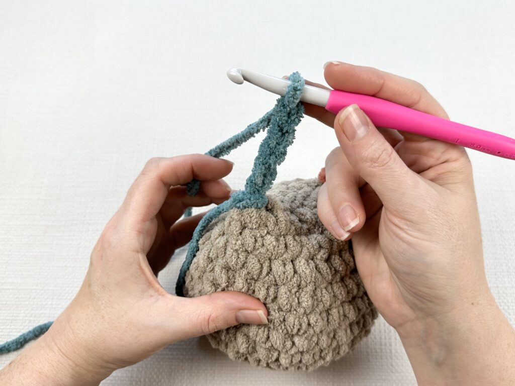 Hands crocheting a rooster tail on the original Mabel chicken pattern. 