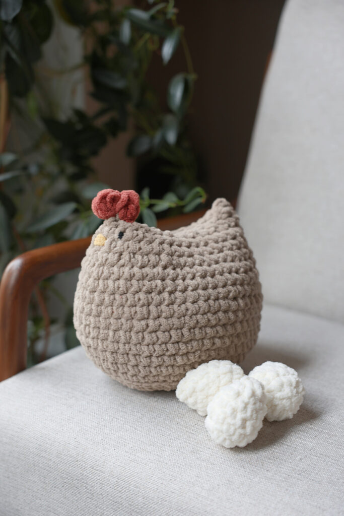 Big crochet chicken sitting on a chair with crochet eggs.