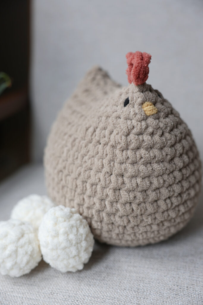 Big crochet chicken sitting on a chair with crochet eggs.