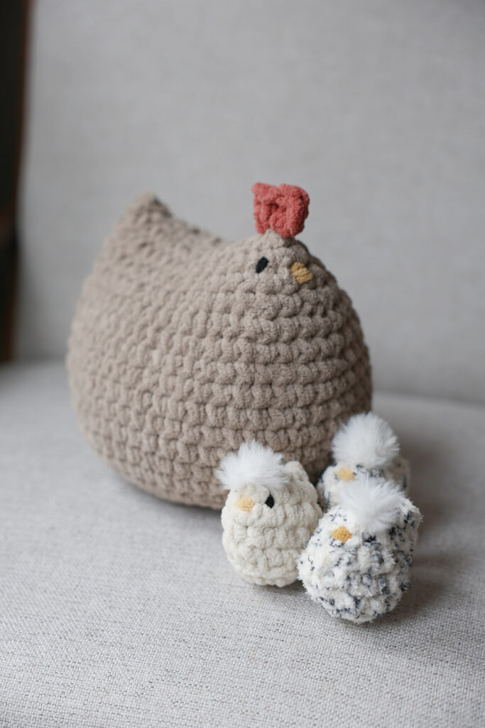 Big crochet chicken sitting on a chair with crochet babies.