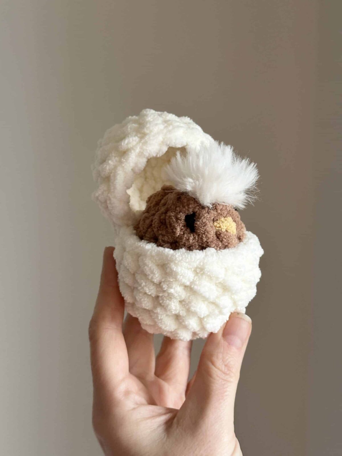 Hand holding a little crochet chick in a hatching egg.