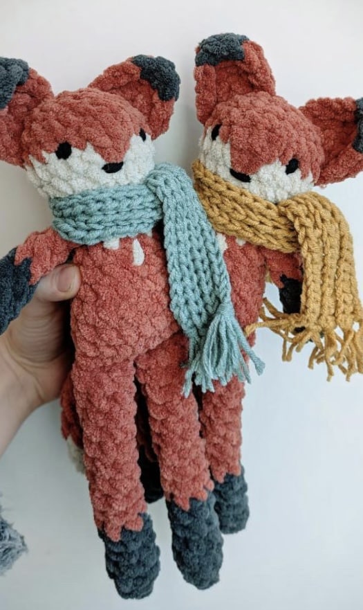 Two crocheted foxes with fable scarfs on.