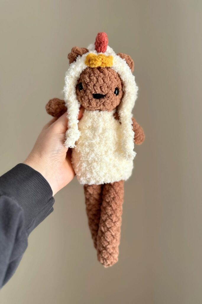 Hand holding a little crochet bear wearing a chicken costume.