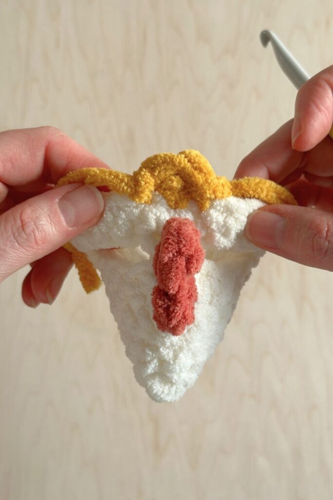Hands holding the chicken hat showing how the beak is stitched into the chicken hat.