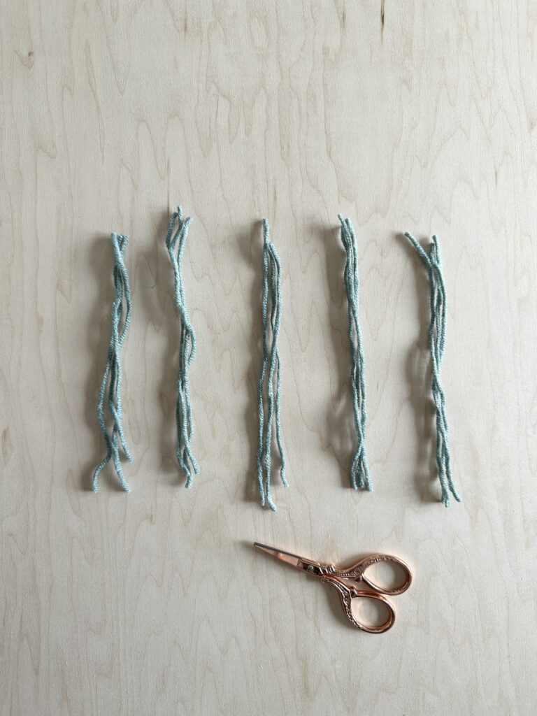 Five prepared tassels for a crocheted scarf with gold scissors beside.