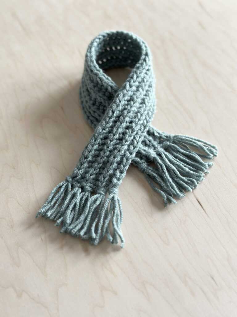 Finished cozy crocheted scarf on a wooden board.