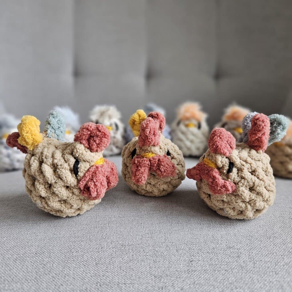 Three crocheted roosters on a chair with seven behind them out of focus.
