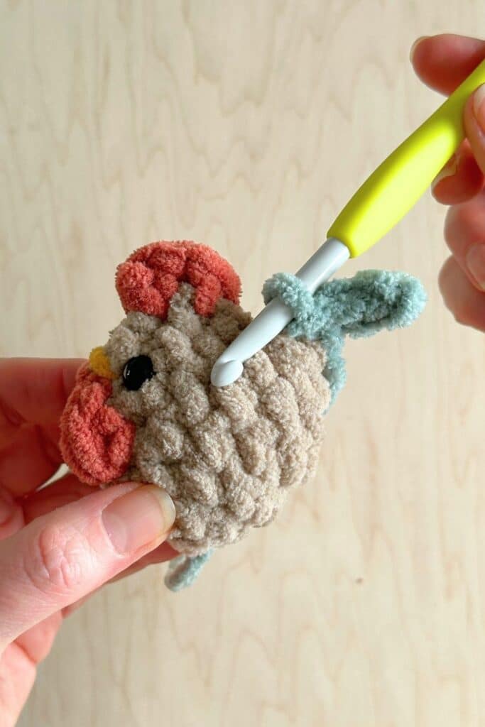 Close up of a crochet hook and hand performing the final step in making the rooster's tail feathers.