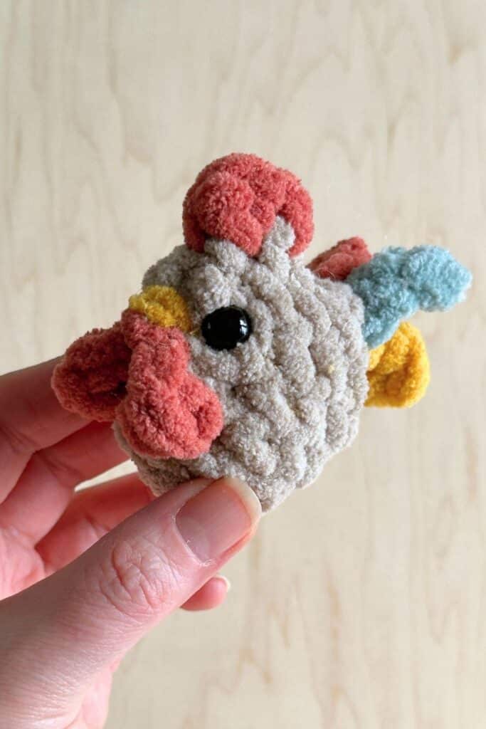 Mini crocheted rooster in a hand looking at front.
