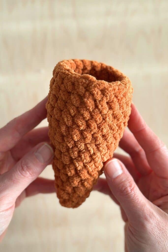 Hands holding the bottom half of a crochet carrot.