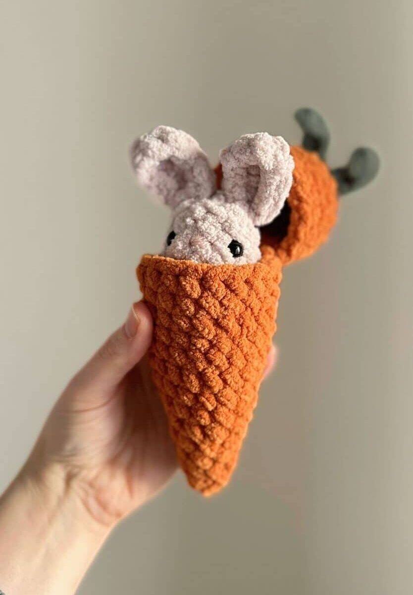 Hand holding an orange crochet carrot "hatched" open to reveal a tiny crochet bunny.