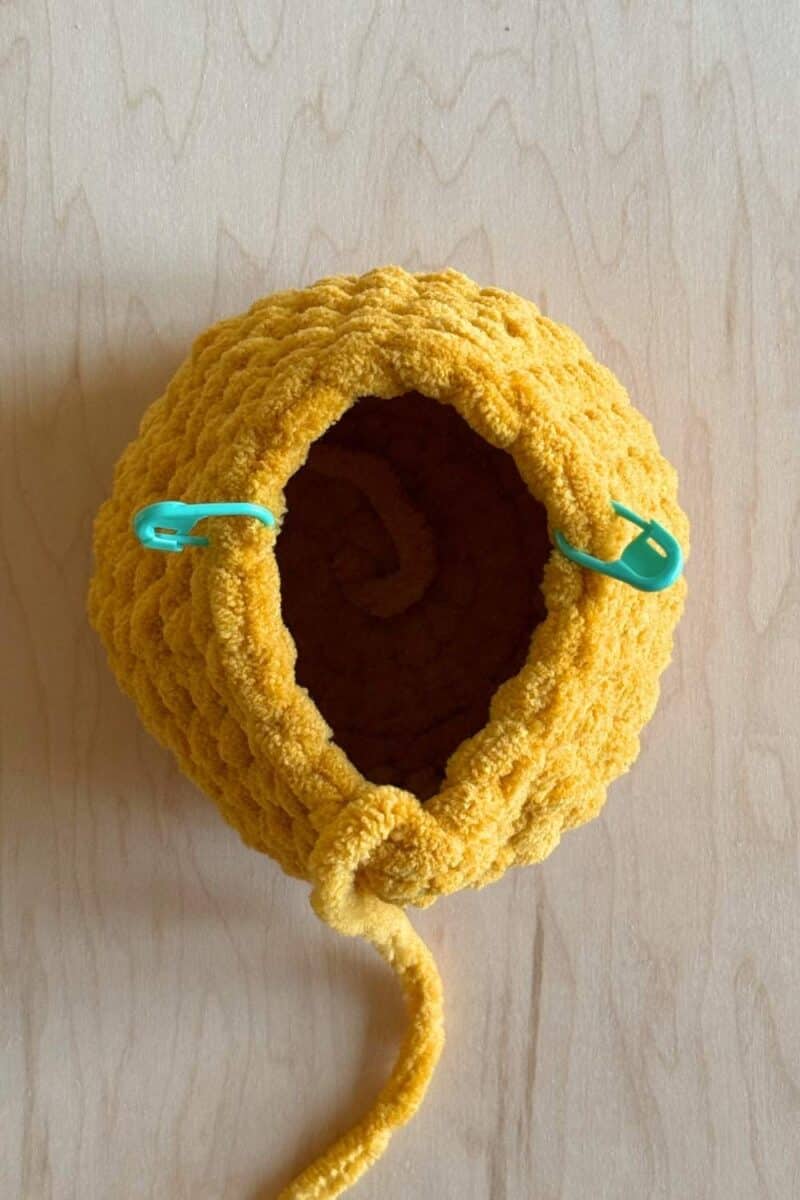 A process photo of a yellow crochet duck. It's showing stitch marker placement. 