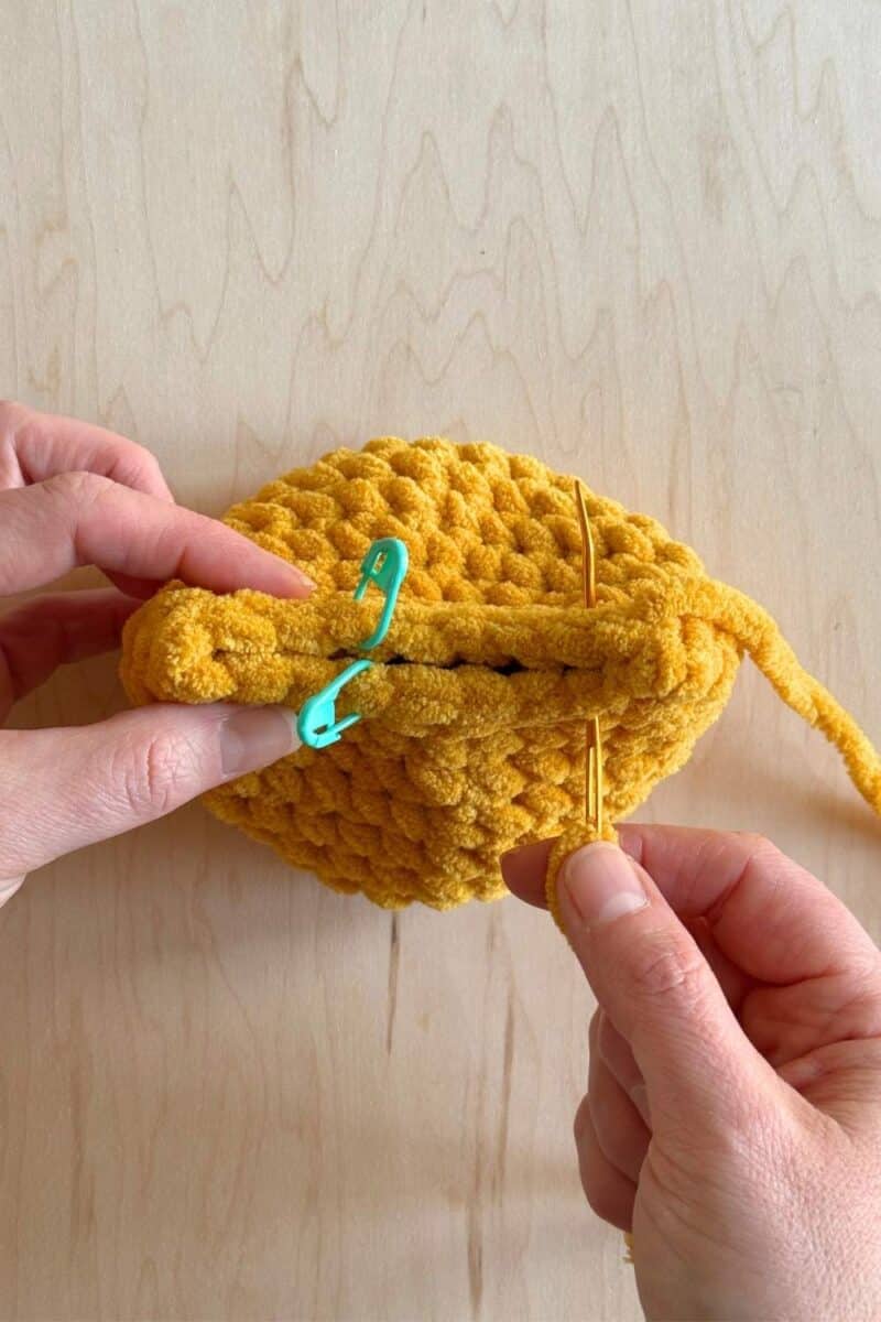 A process photo of a yellow crochet duck. It's showing a yarn needle sewing the back shut.