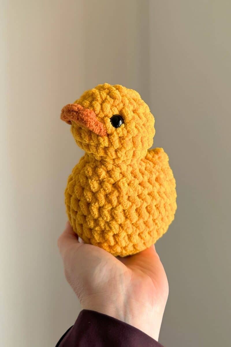 A hand holding up a yellow crochet duck. 