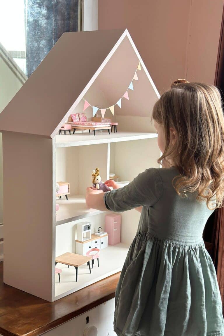 A child in green playing with a pink and white Fable Collection Dollhouise.
