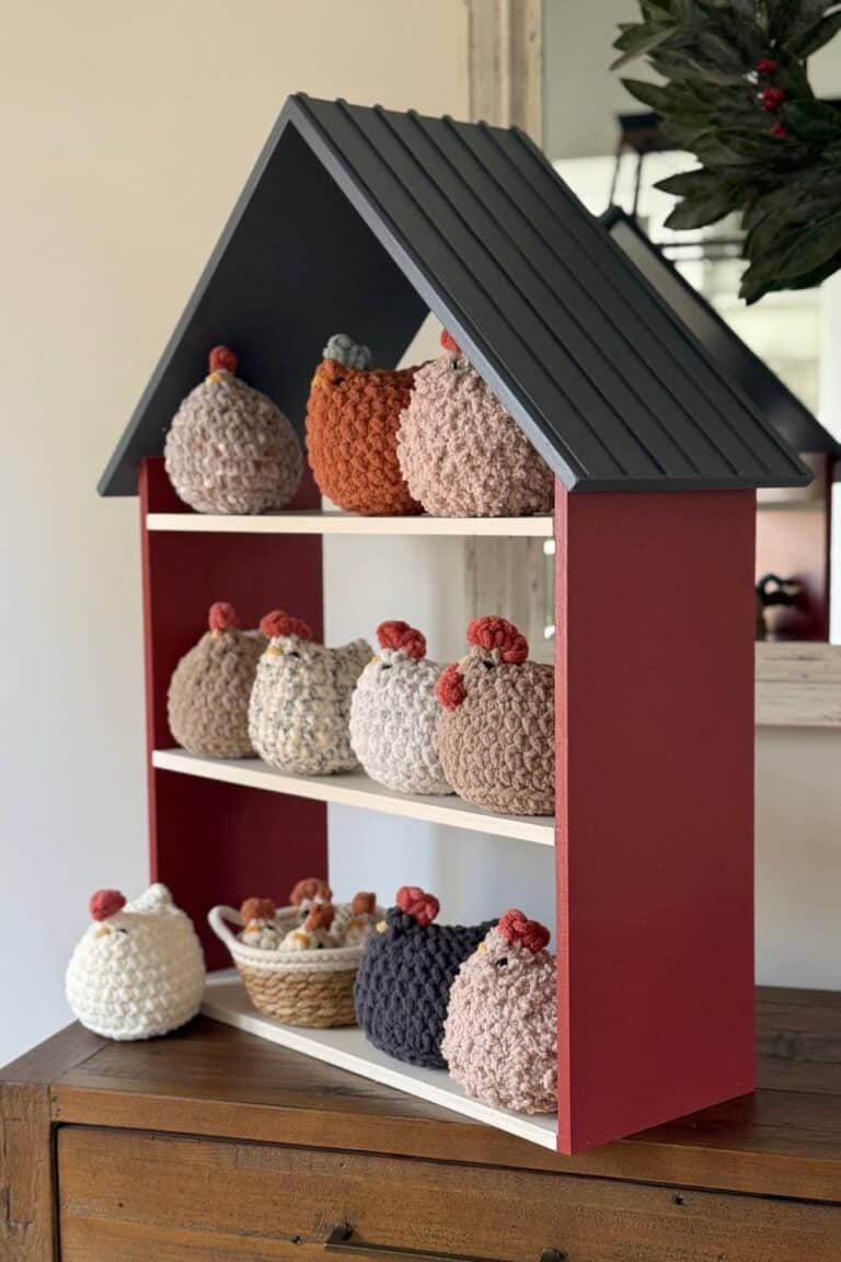 A Red and Charcoal colored Mabel Chicken Market Coop sitting on a table full of crochet Mabel chickens in a variety of colors and textures.