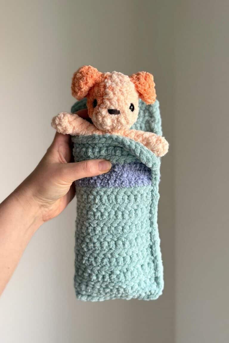 Hand holding a crochet sleeping bag with a little crochet dog inside.