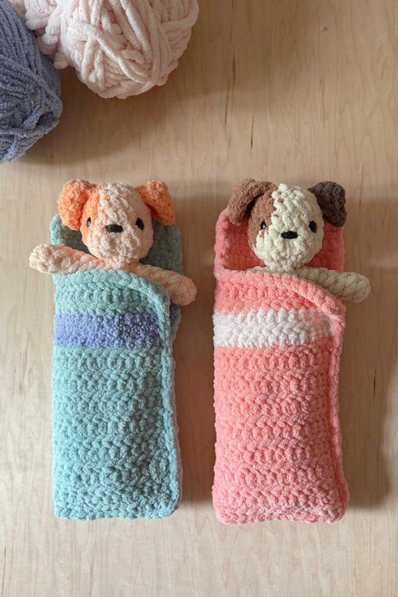 Two crochet sleeping bags in blue and pink with crochet dogs inside.
