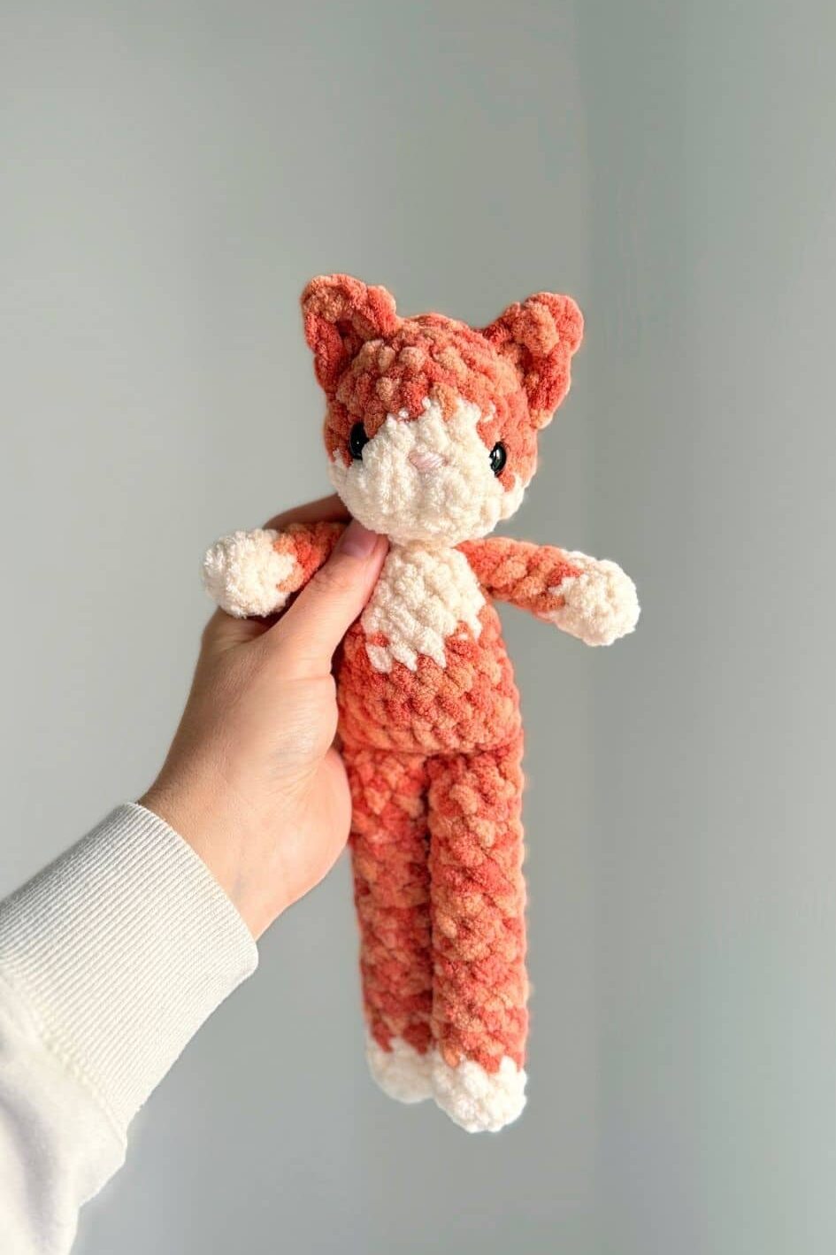 Hand holding the finished crochet cat - this image shows a full-body image of the cat. 