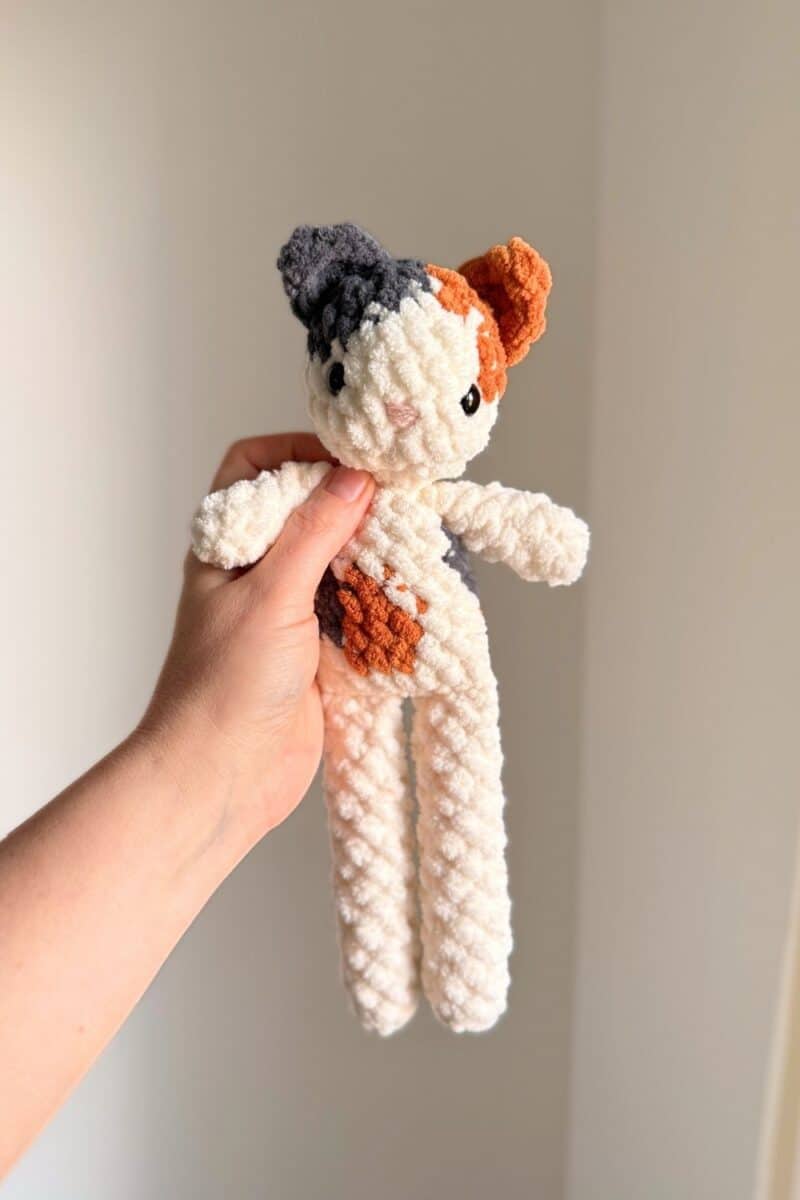 Hand holding a crochet calico cat.