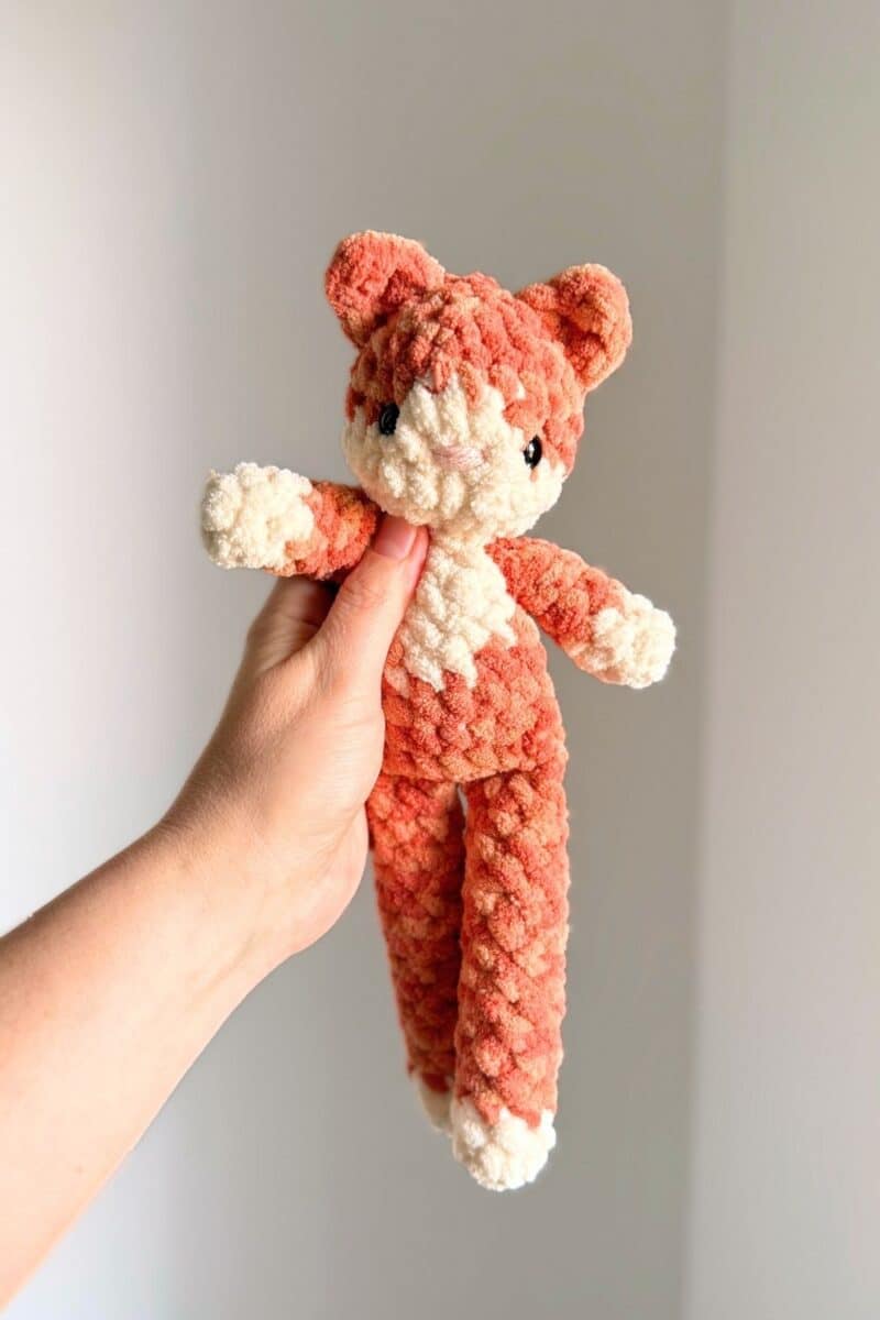 Hand holding a crochet orange and cream colored cat.