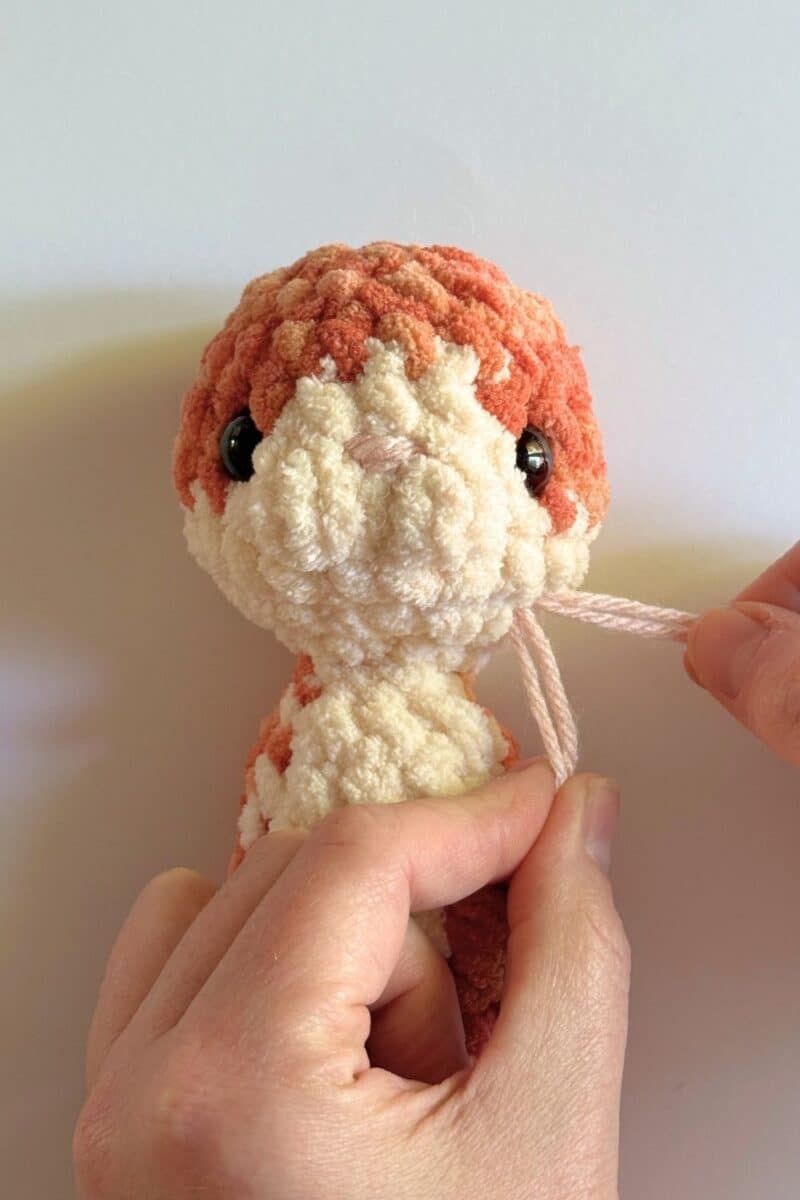 Process photo showing where to place the nose on a crochet cat's face. 