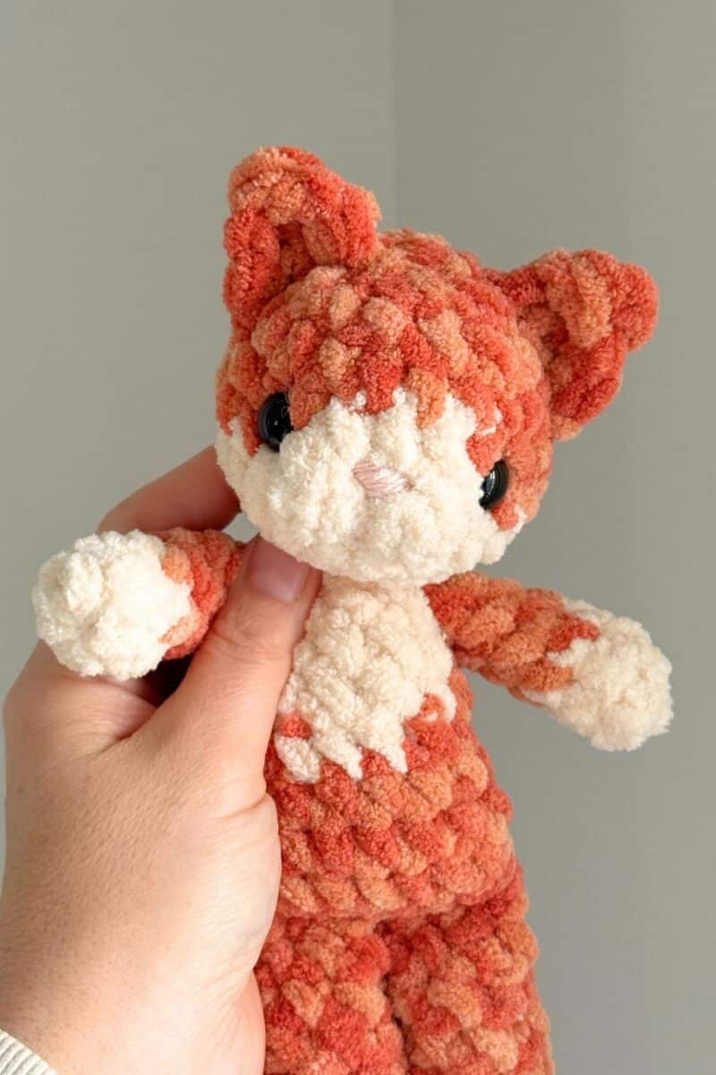 Hand holding the finished crochet cat - this image shows a close-up of the face detail.