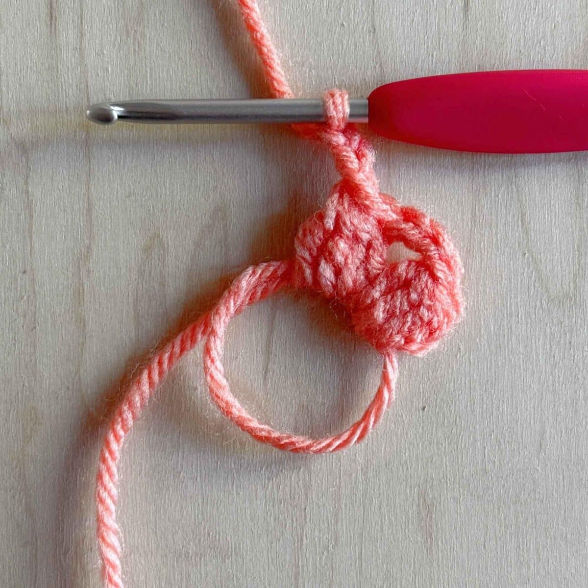Second step (shown in pink yarn) of making round 1 of the crochet square. Photo showing two clusters.