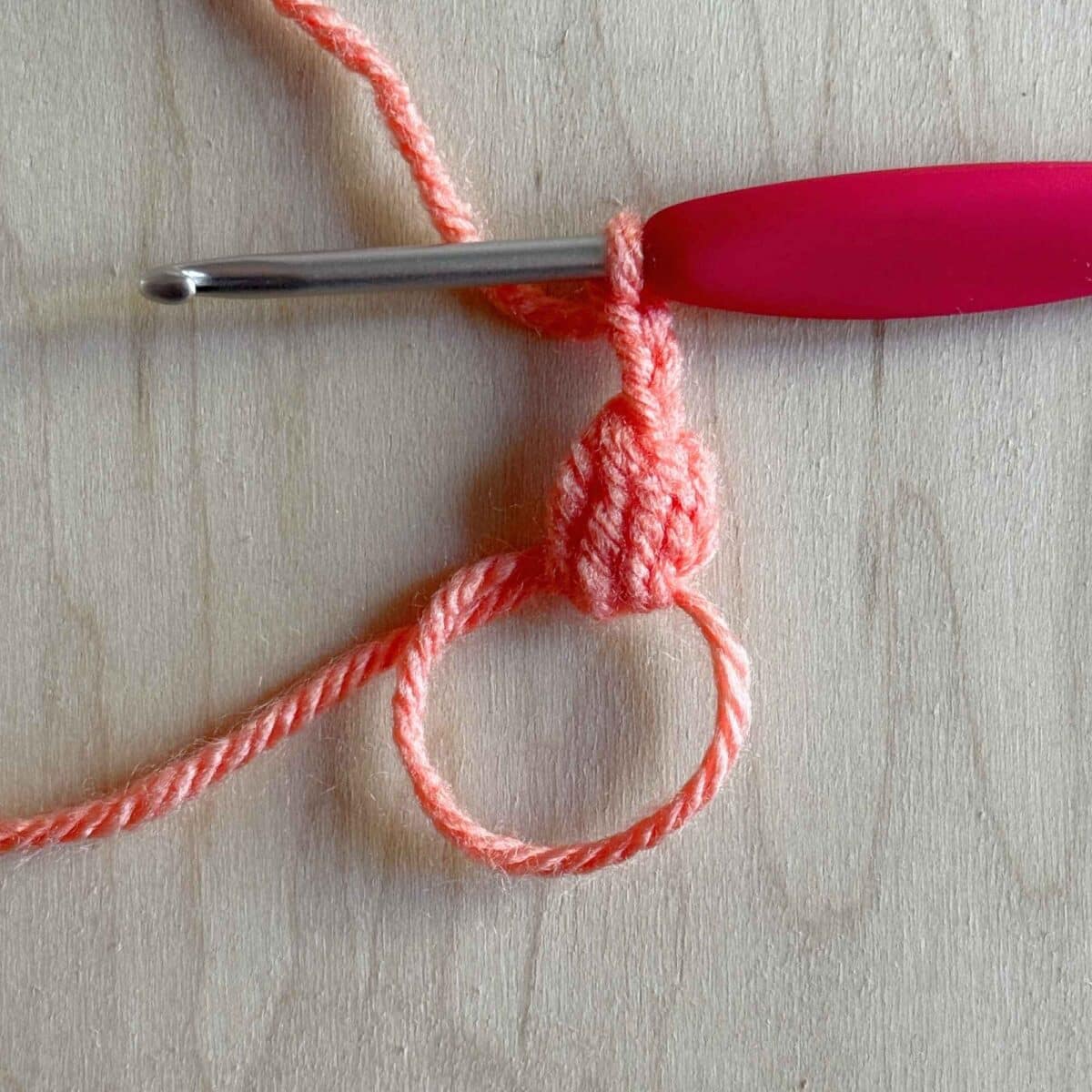 First step (shown in pink yarn) of making round 1 of the crochet square.