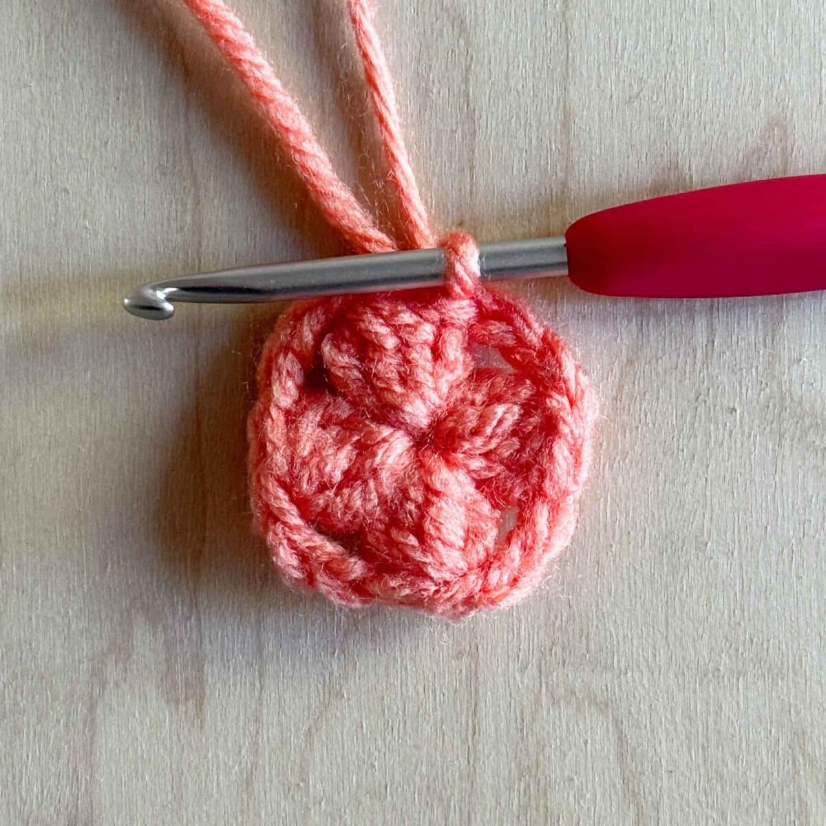 Third step (shown in pink yarn) of making round 1 of the crochet square. Photo showing all four clusters pulled together.