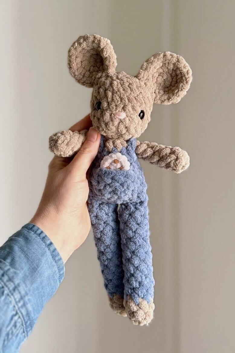 Hand holding a crochet mouse wearing blue overalls with a little tiny crochet cookie in her pocket.