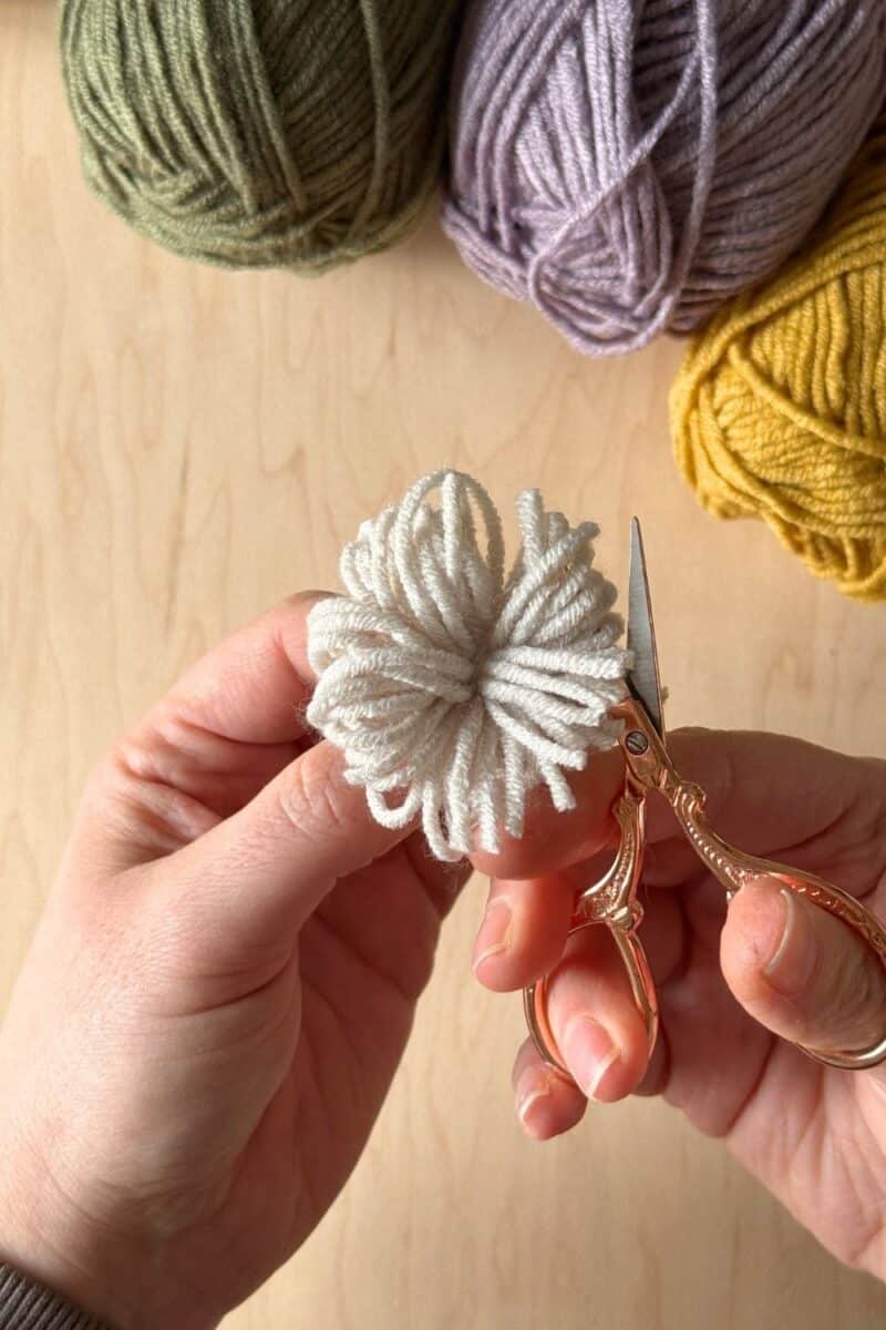 Hands snipping the loops on the pom pom.