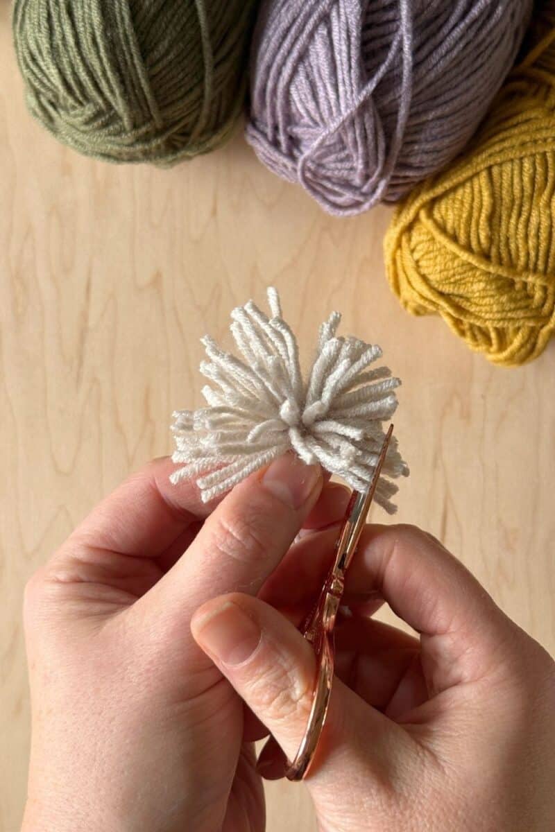 Hands snipping the loops to shape them for the pom pom.