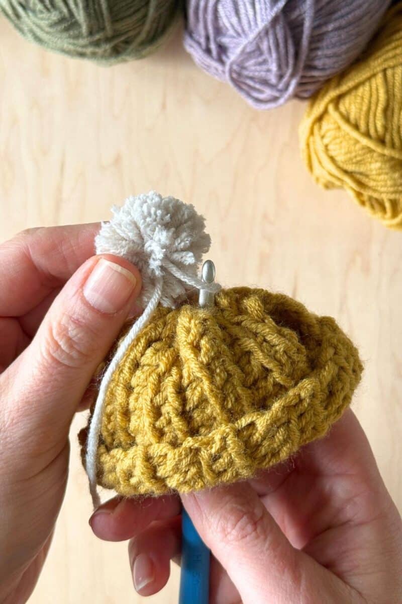 Hands using a crochet hook to weave the tails into the hat to secure.