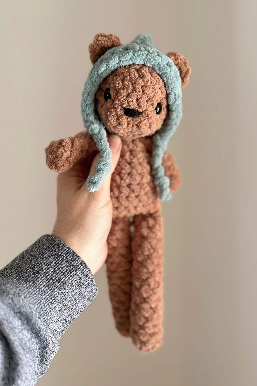 hand holding a brown crochet bear wearing a blue hat.