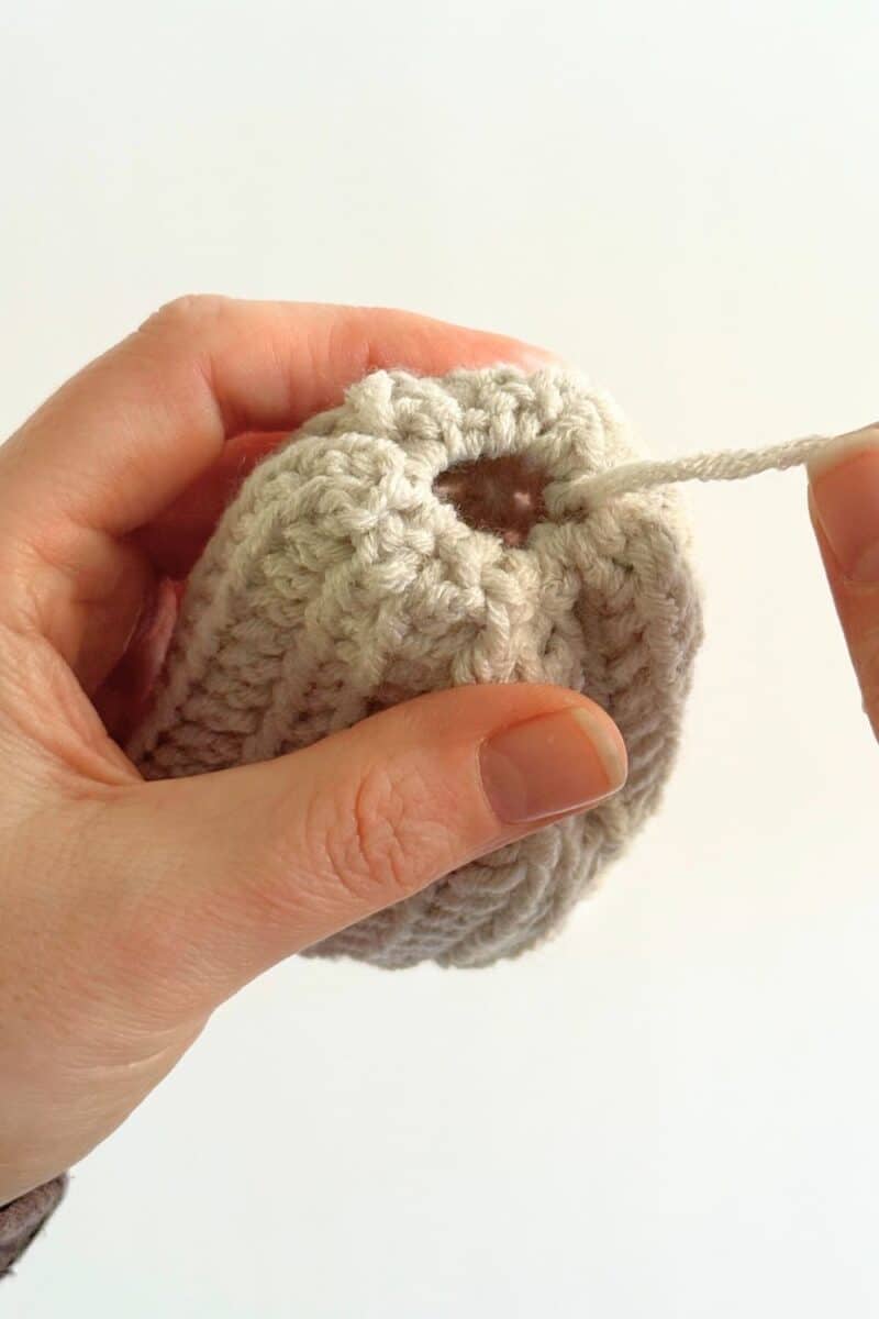 Hand pulling the yarn tail to close the top of the hat.