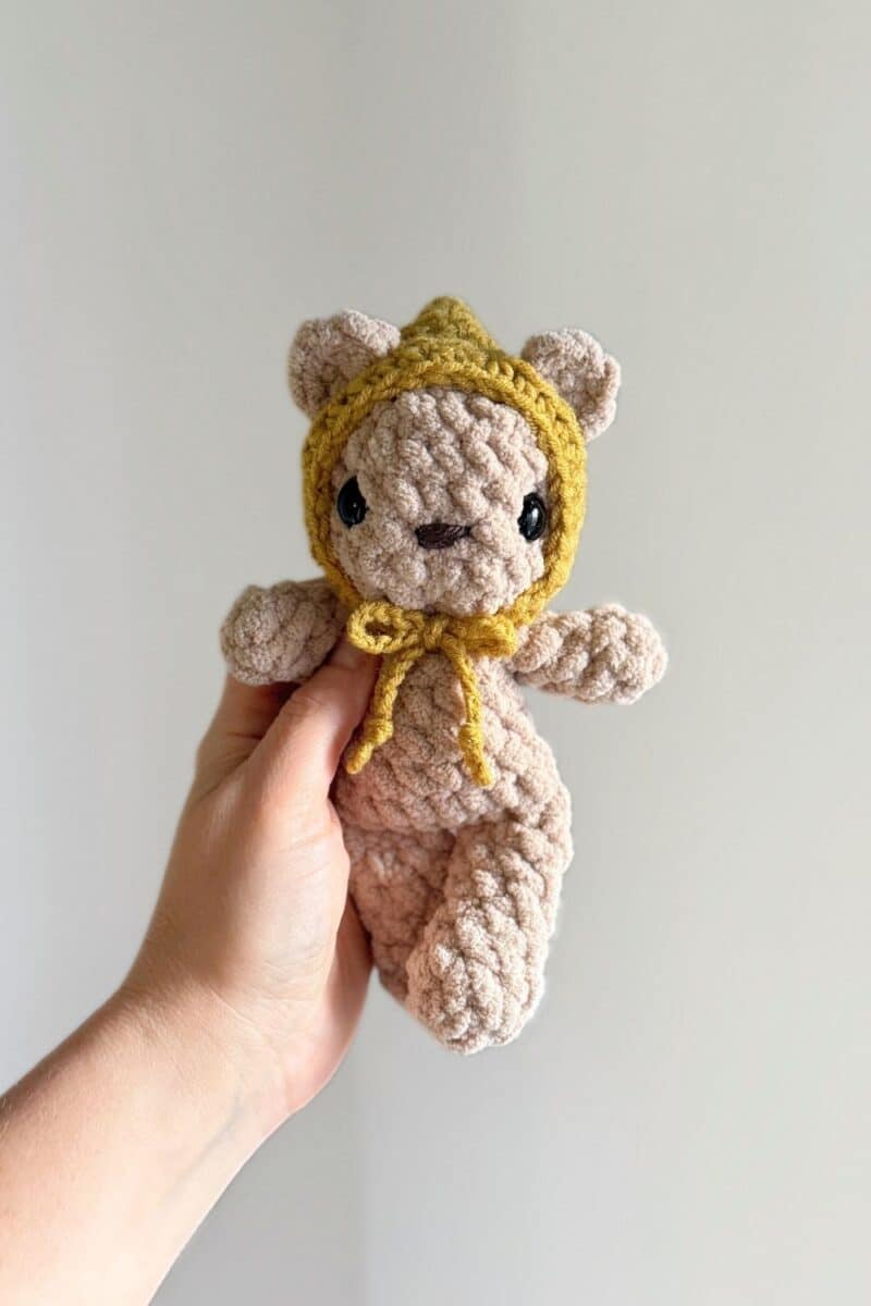 Hand holding a brown crochet bear wearing a green hat.