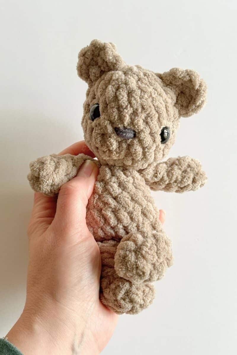 Hands holding a tiny light brown crochet bear.
