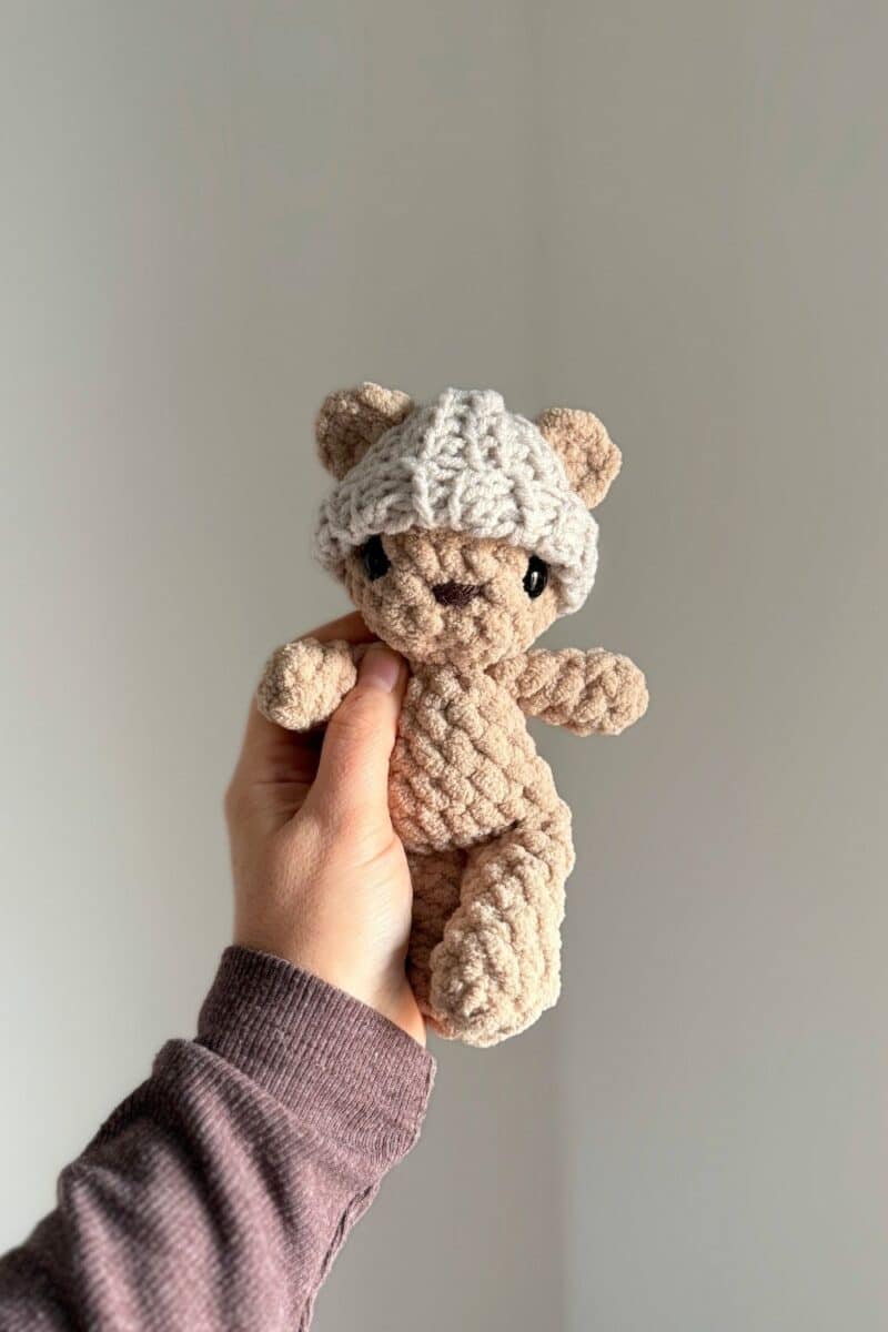 Hand holding a crochet bear wearing a little crochet hat or beanie. 