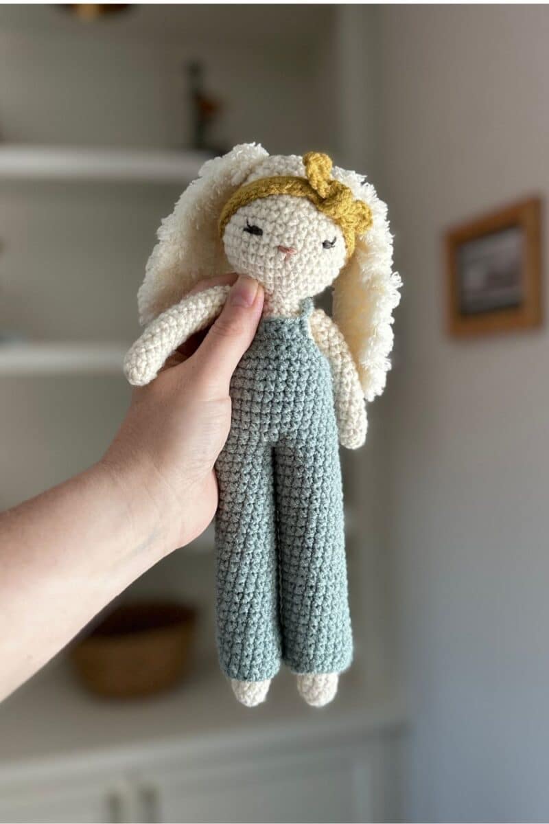 Hand holding a crochet bunny wearing overalls and a headband.