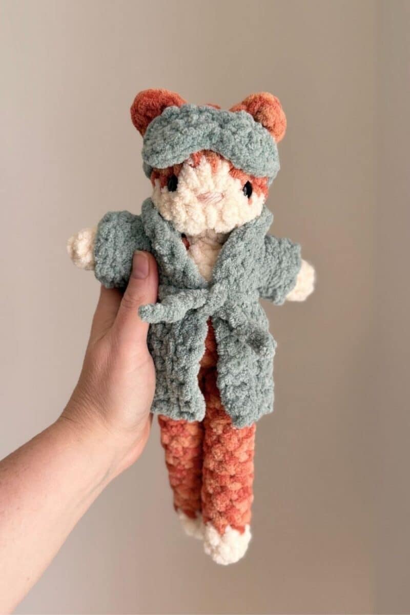 An orange crochet cat wearing a robe and eye mask.