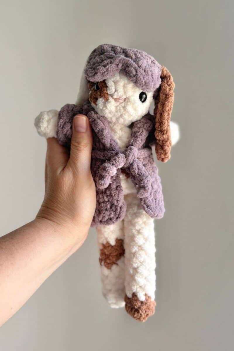 A spotted crochet bunny wearing a purple robe and eye mask.