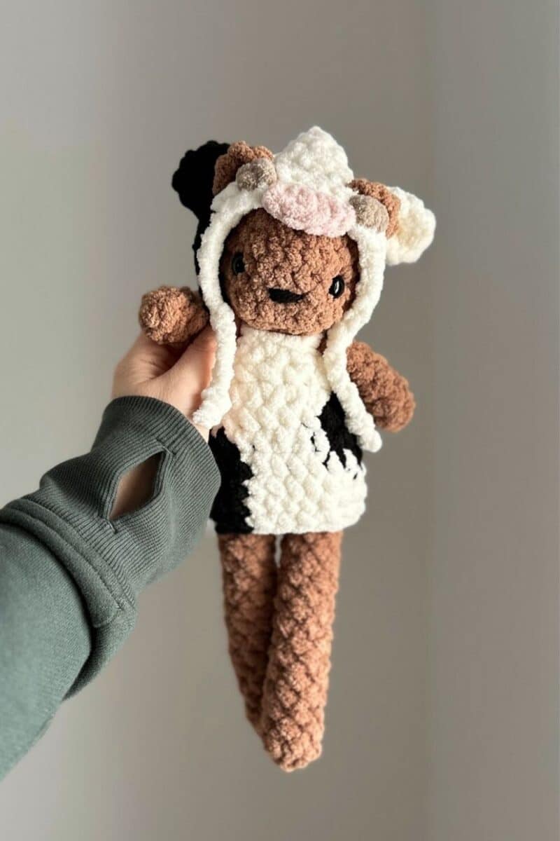 Hand holding a brown crochet bear wearing a crochet cow costume.