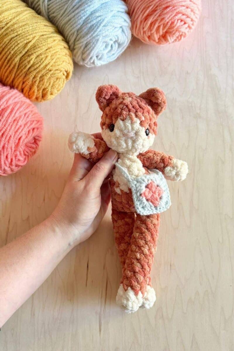 An orange crochet cat wearing a tiny crochet purse.